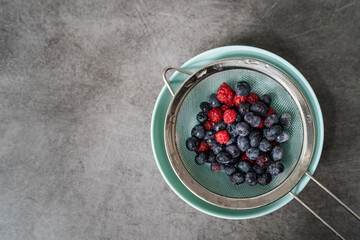 Top down view on blueberries and raspberries in plate on the kitchen counter - fresh organic fruit washed and ready to eat - healthy eating concept copy space