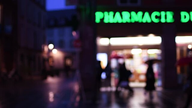 Main facade of Pharmacy drug store - Defocused view of a French street with few pedestrians during national lockdown due to COVID-19 coronavirus pandemic