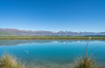 Idyllic South Island landscape reflected in calm Ohau Canal at sunrise.
