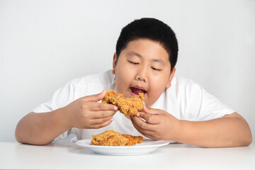 Asian fat boy eats fried chicken Wear a white shirt. Concepts of child health problems Pathogenic...