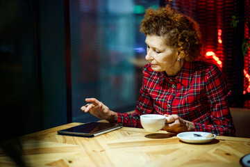 Fototapeta na wymiar Senior woman using tablet in a cafe. Mature woman relaxing at a restaurant with tablet pc. Elderly female use digital tablet at coffee shop. Technology, old age and people concept. Mature student