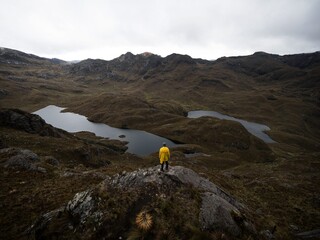 Person in yellow jacket infront of Andes hills tundra grassland lakes landscape in El Cajas...