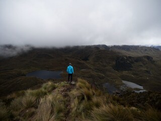 Person in blue jacket infront of Andes hills tundra grassland lakes landscape in El Cajas National...