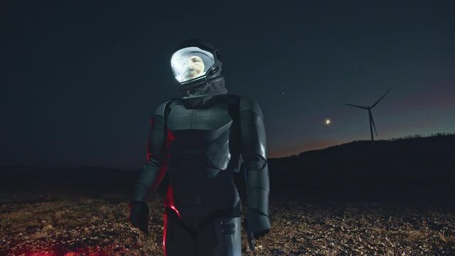 Astronaut using transparent future device holographic virtual touchscreen while walking through the field with windmills and exploring new planet at the night. Surreal, explore, new live, nightlife