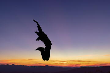 Silhouette of happy girl jumping playing on mountain at sunset
