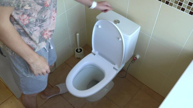 The man lowers the toilet seat and flushes the water