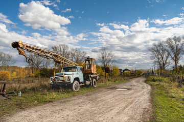An old Soviet truck crane stands on the side of a village road