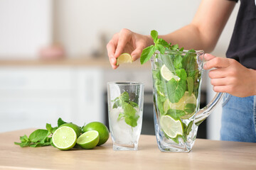 Female hands with jug of fresh mojito on table in kitchen