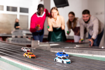 Models of race cars on the track in playroom, players on background, selective focus on car