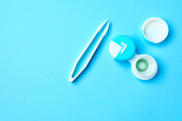 Container with contact lenses and tweezers on color background
