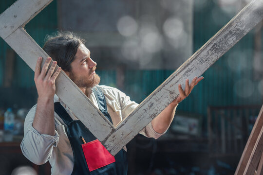 carpenter in wood workshop selecting wooden frame for his workwood