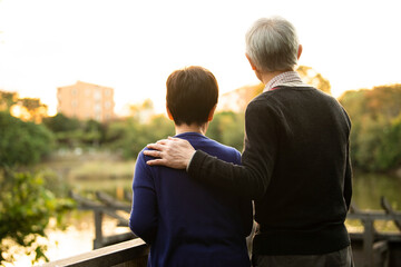 夕日の綺麗な公園で仲良く寄り添う高齢者の夫婦