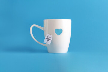 Blue monday tea text with sad smiley face on white cup with blue heart on blue background. The most depressing day of the year. Blue monday breakfast concept. 