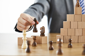 Businessman in a suit arranging chess pieces on wooden blocks on different levels