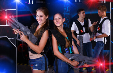 Portrait of two positive girls with laser guns in their hands in dark laser tag room