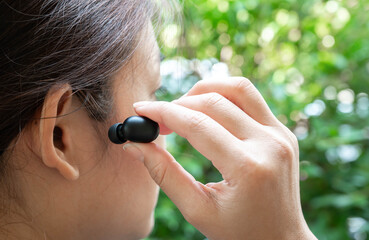 Close up of woman is using the black true wireless earbuds by hand to put in ear and control