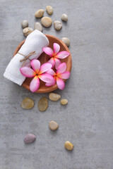 Spa composition with pink frangipani flowers and towel, salt in wooden bowl ,stones on grey background

