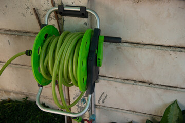 Green roll watering hose stuck to the concrete wall