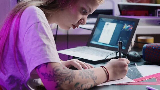 Young woman tattoo artist draws sketch for tattoo in studio in front of laptop