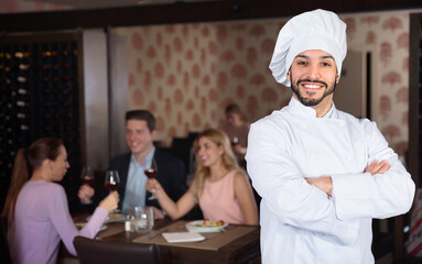 Portrait of cheerful positive smiling handsome professional chef on background with restaurant guests