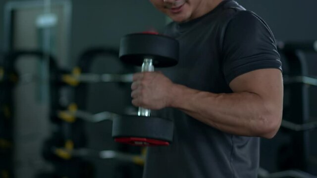 B-roll footage, muscular Asian young man lifting up a dumbbell in gym. Practice body and muscle building for a good body shape and poser.