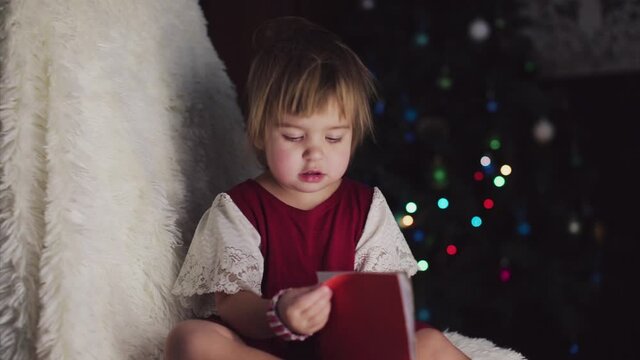 a child in red clothes is sitting waiting for the new year. the concept of celebrating Christmas at midnight. holiday costume. a girl writes a letter to Santa Claus. wish list