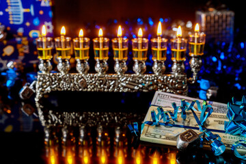 Dollar bill gift with burning menorah with reflection for Hanukkah.
