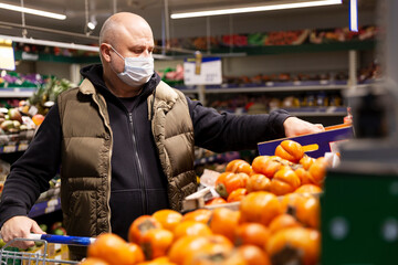 A man in a medical mask picks seasonal fruits in the store. Coronavirus pandemic.