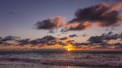 Fototapeta premium Sunset over the Black Sea. In the evening sky, pink and purple clouds. The waves are foaming on the beach. Sunny path.