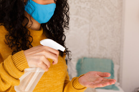 Mixed race woman wearing a face mask disinfecting hands with spray