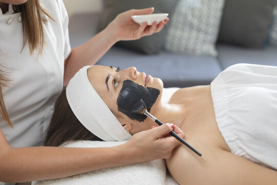 Caucasian woman lying back while beautician applies a face mask
