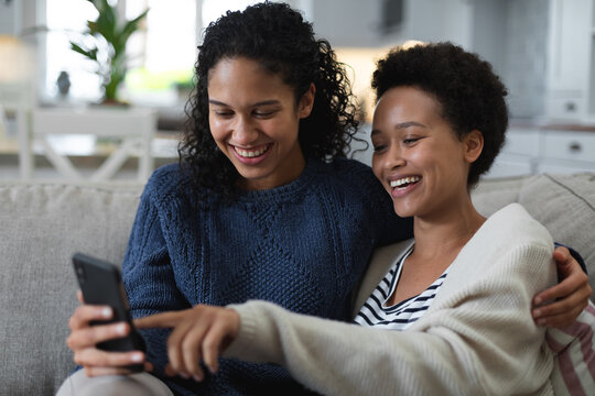 Mixed race lesbian couple sitting on couch using smartphone