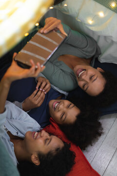 Happy mixed race lesbian couple and daughter lying down using smartphone