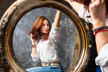 Beautiful young woman looking on her reflection at the mirror