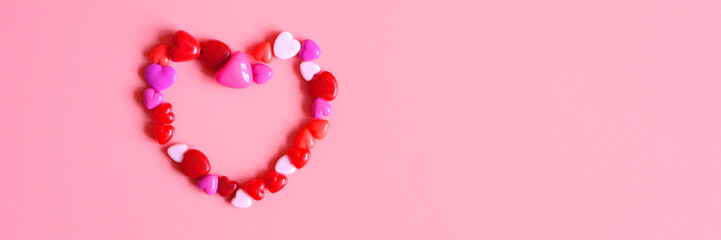 Obraz premium a heap of heart form glossy beads in different pink shades laid out in the shape of a heart on a pink background. banner. space for text