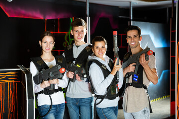 Fototapeta na wymiar Group portrait of friends girls and guys with guns in their hands in dark laser tag room. High quality photo