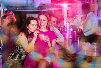 Chatting friends holding cocktails and laughing in nightclub. High quality photo