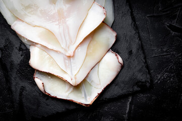  Raw peeled squid on a slate board and black background. Top view, copy space