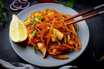  Funchoza with spicy sauce and squid on a black background. Glass noodles, Asian food.