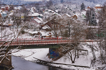  A snow-covered village on the Bank of a river that is crossed by a road bridge.