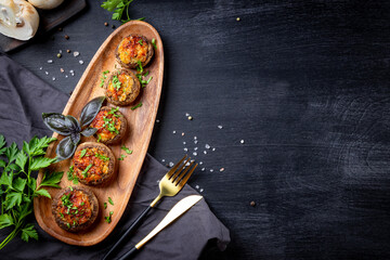  Baked stuffed mushrooms on a wooden plate and black background, top view, copy space