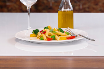 Selective focus of a plate with pasta salad and a fork, with an out of focus bottle of oil at the back. Pasta and healthy food concept.