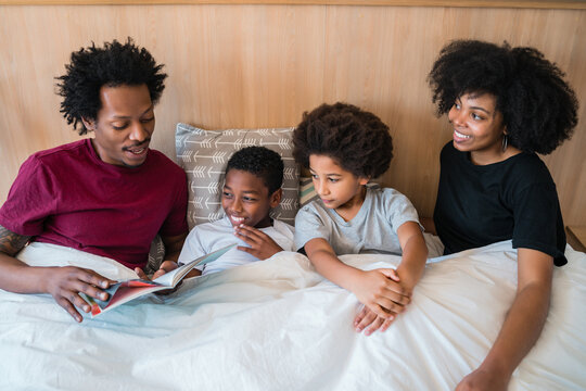 Family reading a book on bed at home.