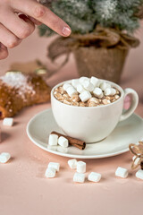 Hand points to a cup of coffee with marshmallows