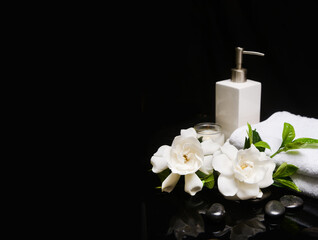 Obraz na płótnie Canvas beautiful spa concept of two white gardenia flower and green leaf and towel, candle,oil bottle on pile of black zen stones 