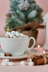 Mug with marshmallows and burning candles on the background of a Christmas tree