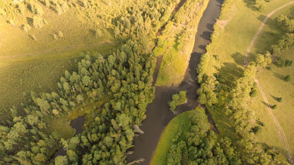 Aerial view from drone over curve river, meadow, country road and dense forest.