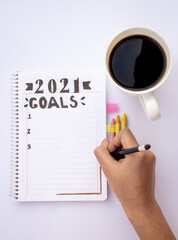 Decorated notebook for writing New Year's resolutions on a table with a coffee cup on the side and a hand writing.