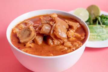 Exquisite Mexican Menudo on a white plate accompanied by a dish with condiments on the back.