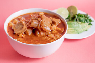 Exquisite Mexican Menudo on a white plate accompanied by a dish with condiments on the back.